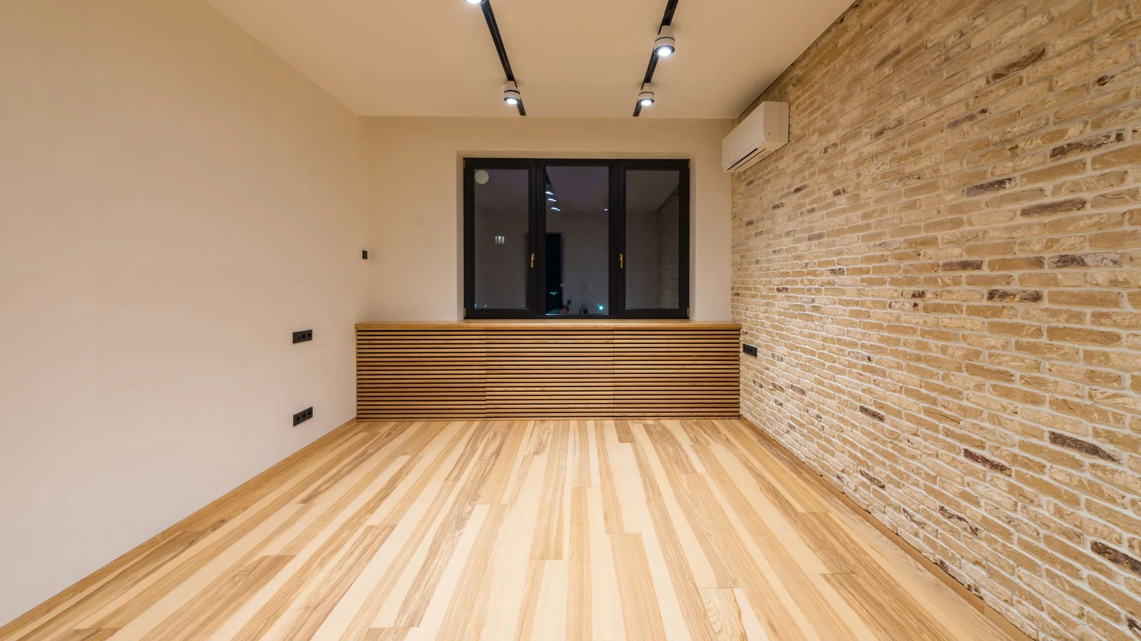 Pièce rénovée au parquet clair, murs blancs et mur de briques apparentes