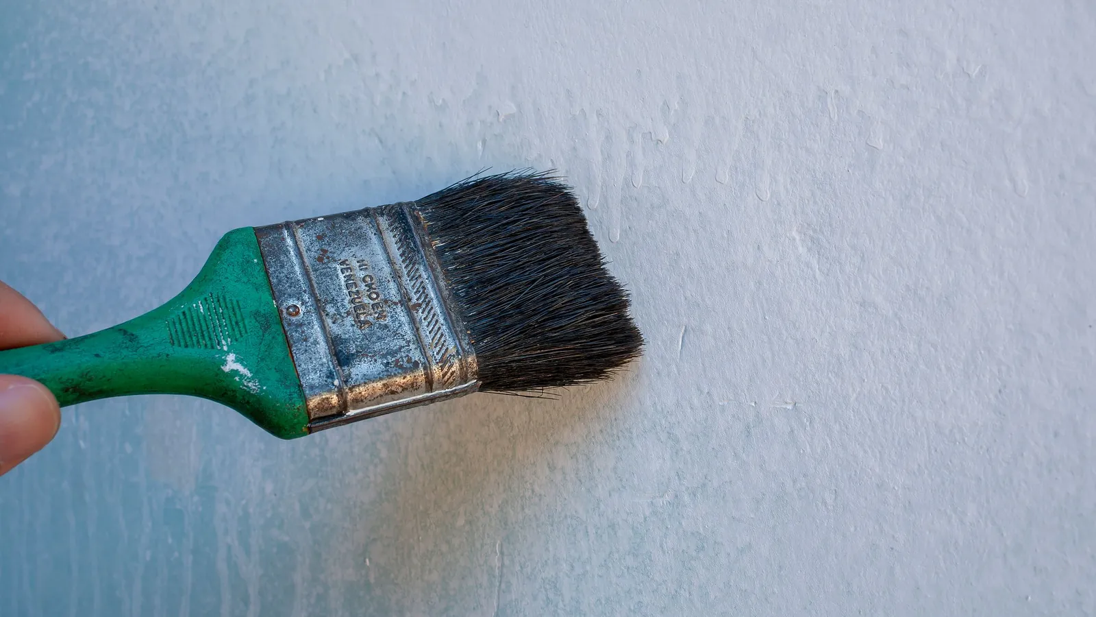 Pinceau appliquant une peinture blanche sur un mur