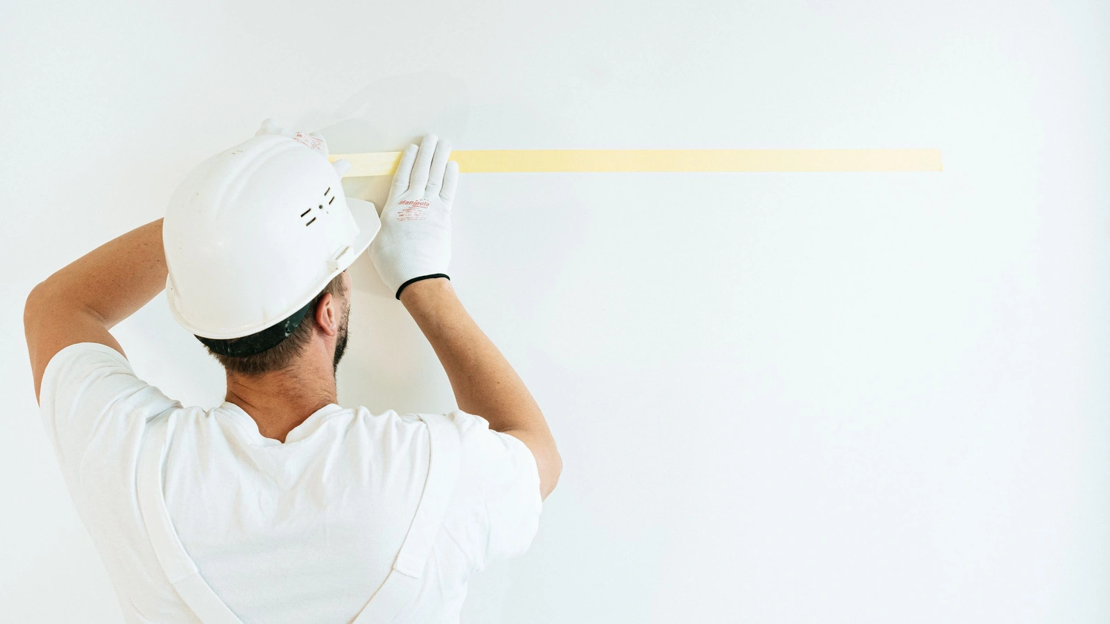 Ouvrier casqué traçant un repère horizontal sur un mur blanc